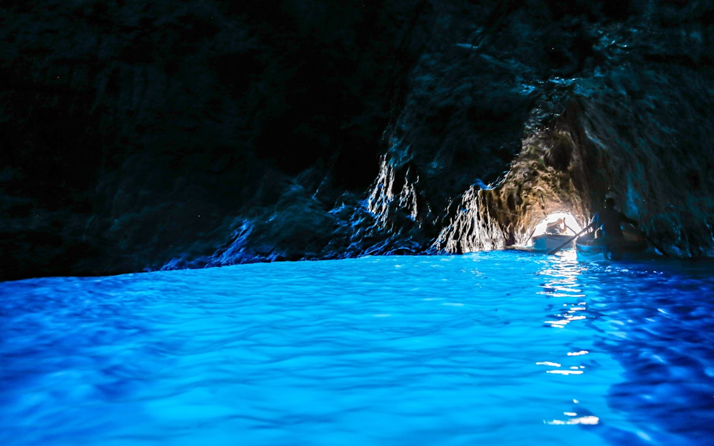 Boat entering Blue Grotto cave with vibrant blue water on Capri, Italy.