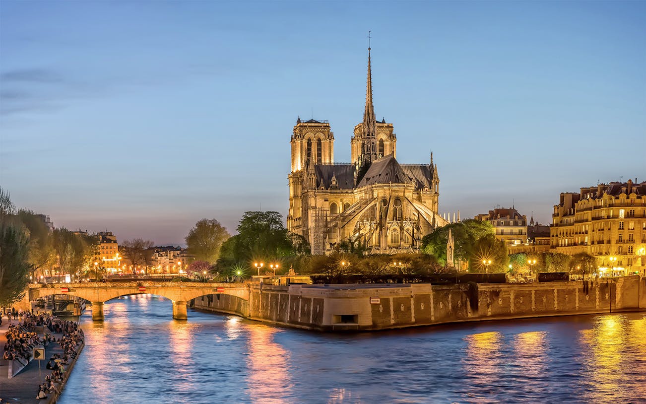 Notre-Dame de Paris illuminated at dusk during city tour along the Seine River.