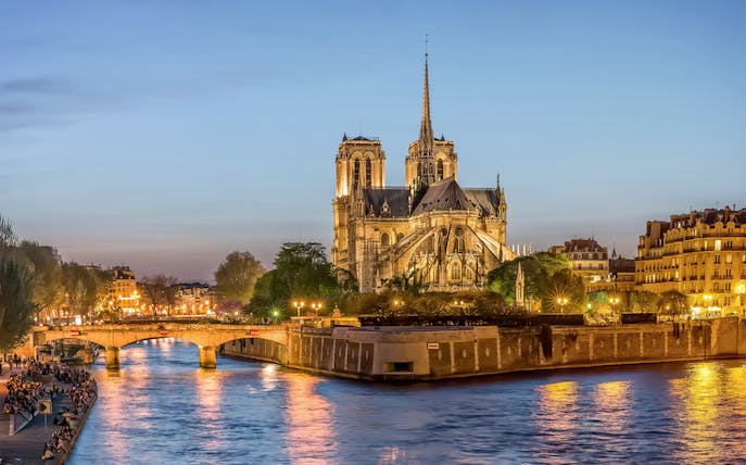 Notre-Dame de Paris illuminated at dusk during city tour along the Seine River.