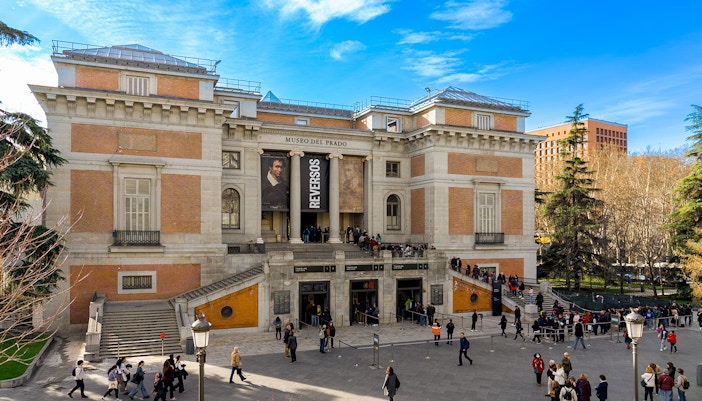 Visitors exploring art exhibits inside Prado Museum, Madrid, during a guided tour.
