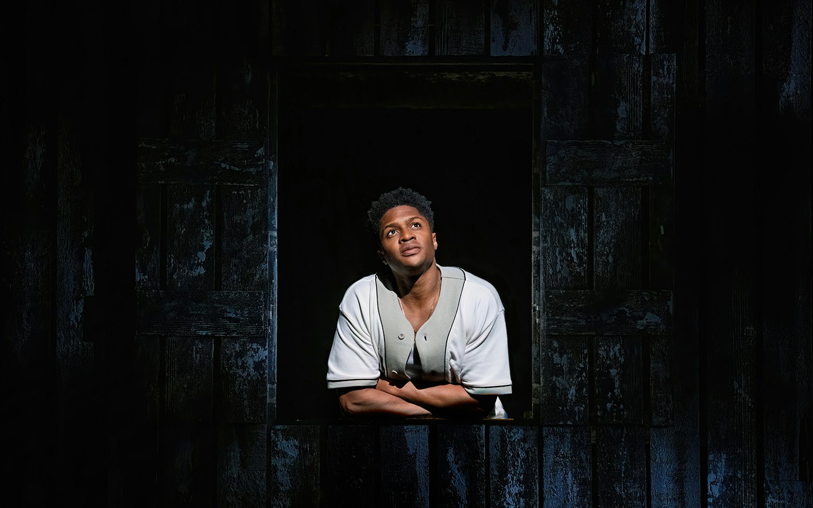 Person in a baseball jersey looking up through a dark window, related to "Our Town" play.