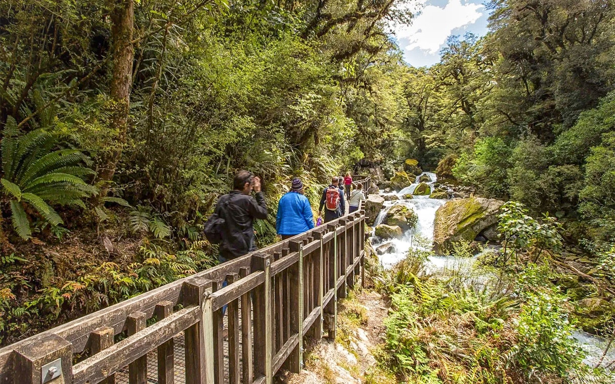 Hikers on Milford Track bridge near waterfall, Te Anau, New Zealand.