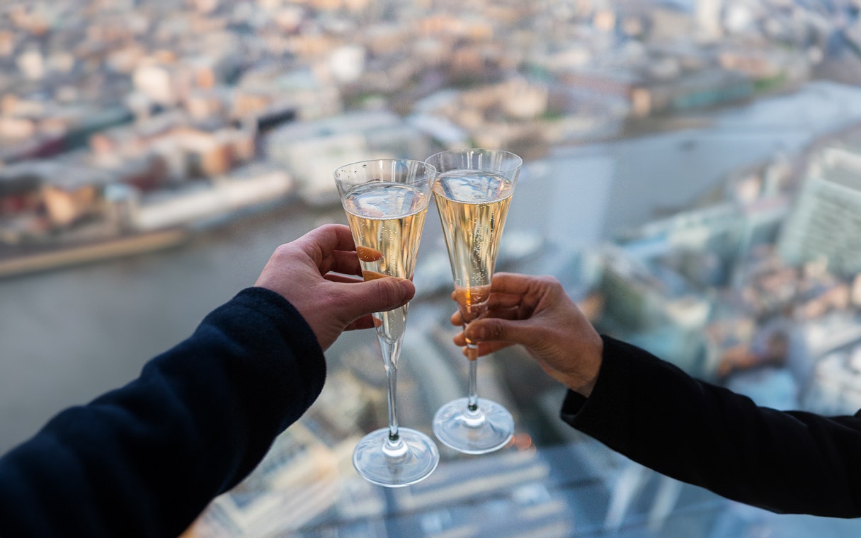 Toasting with champagne at the top of the Shard, London skyline in background.