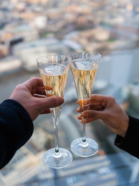 Toasting with champagne at the top of the Shard, London skyline in background.