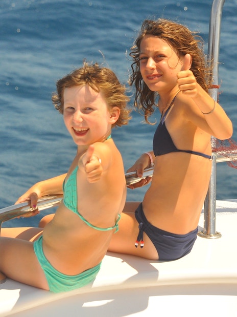 Girls on cruise deck giving thumbs up, watching dolphins in the ocean.