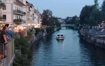 Ljubljana river view with boat and people on riverside, evening city exploration.