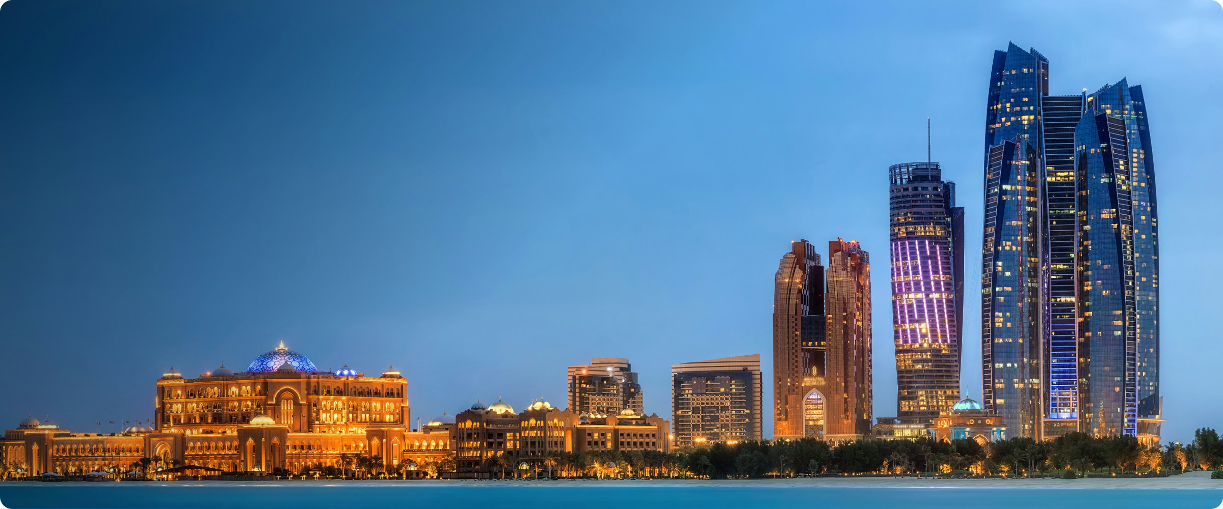 Sheikh Zayed Grand Mosque in Abu Dhabi at sunset with illuminated domes and minarets.
