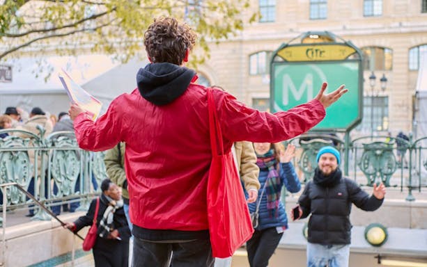 Tour guide leading a group near Notre Dame, Paris, with a metro entrance in the background.
