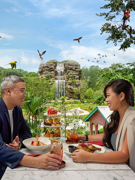 Couple dining at Bird Paradise restaurant with waterfall and birds in view.