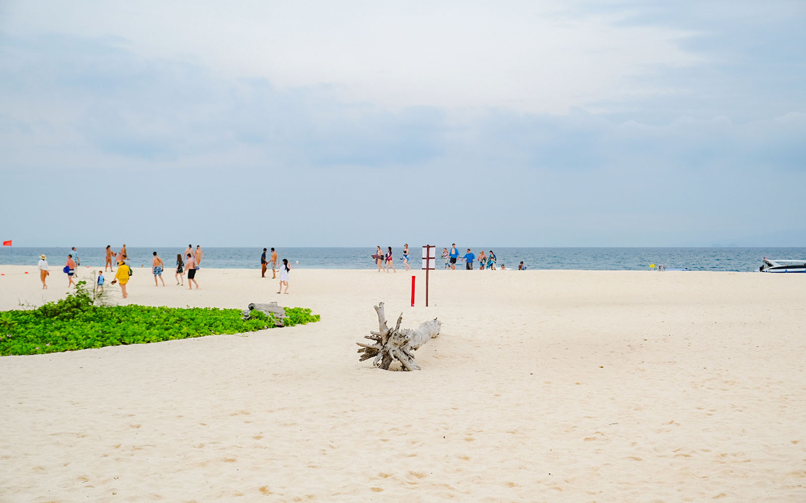 Wide expanse of white sand beach with people walking towards the ocean under a cloudy sky.