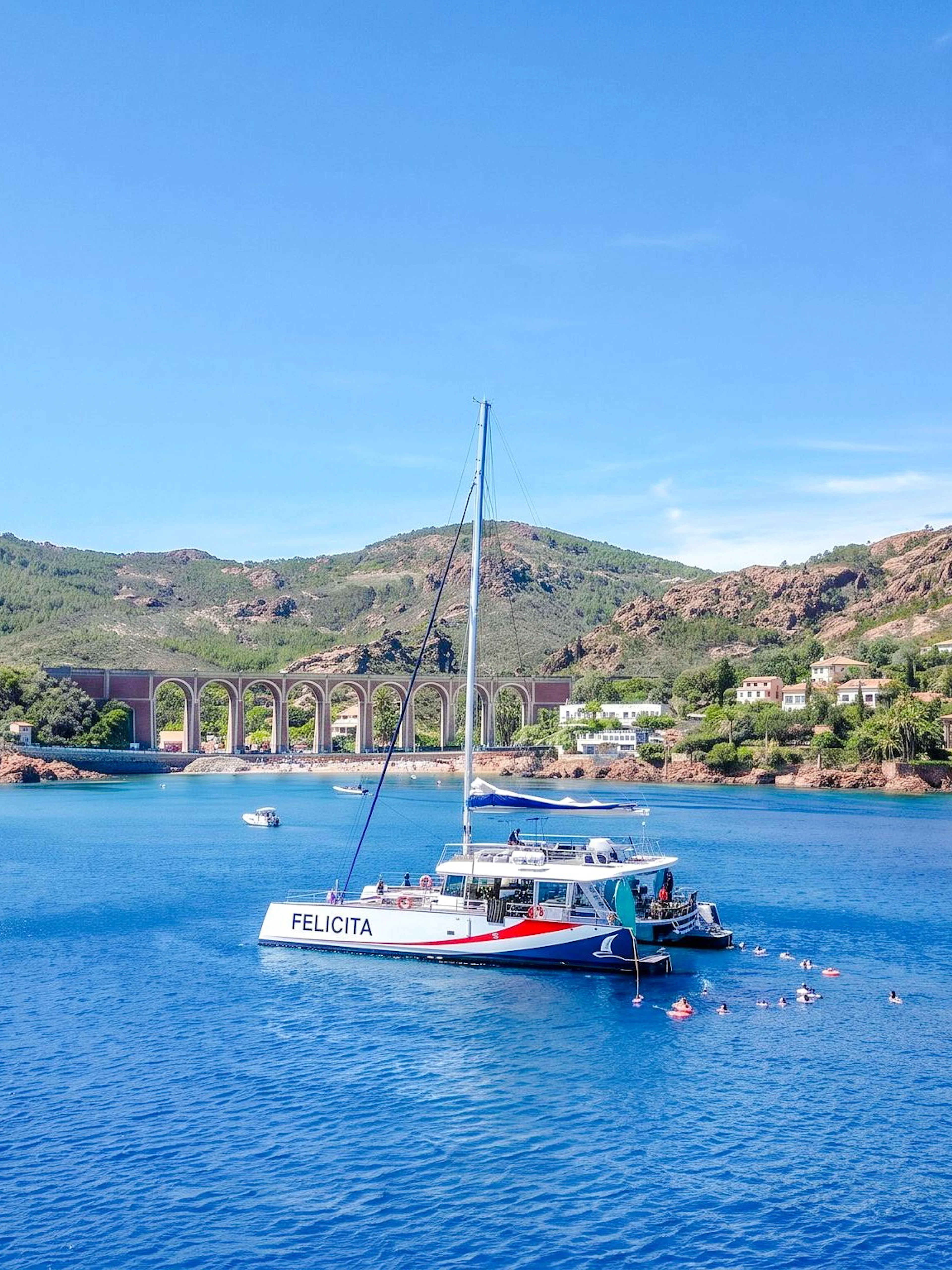Catamaran in Villefranche bay with snorkelers in the water, surrounded by hills and coastal homes.