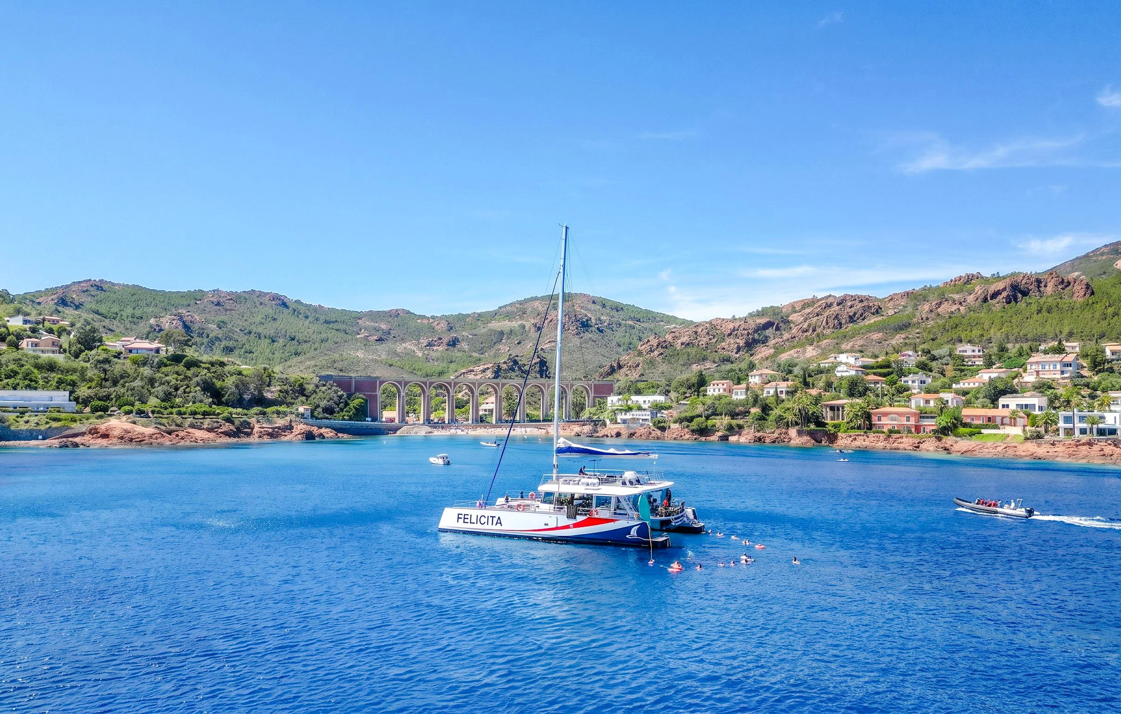 Catamaran in Villefranche bay with snorkelers in the water, surrounded by hills and coastal homes.