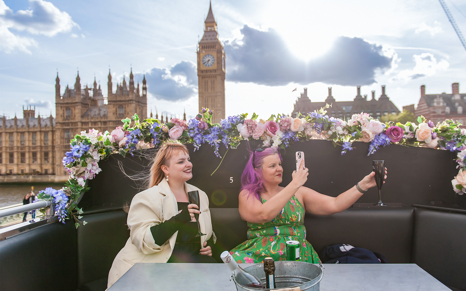 Two women taking photos with drinks on a bus near Big Ben, London.