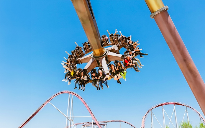 Visitors enjoying a thrilling ride at MagicLand Amusement Park with roller coaster in background.