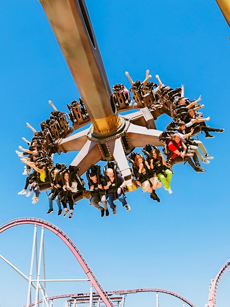 Visitors enjoying a thrilling ride at MagicLand Amusement Park with roller coaster in background.