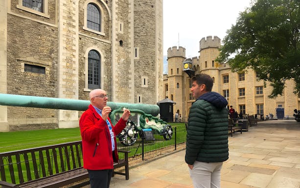 Guide explaining history to visitor at Tower of London courtyard.