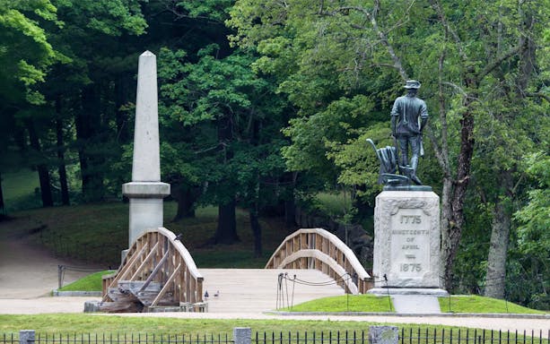 North Bridge and Minuteman Statue in Boston surrounded by trees.