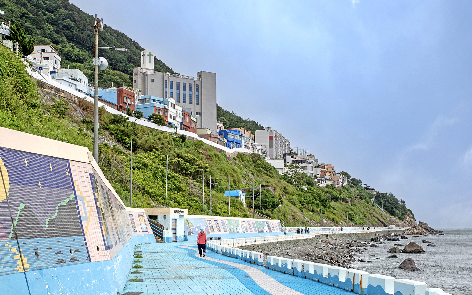 Seaside walkway with colorful murals and hillside buildings in Busan, part of the Blueline Park Sky Capsule Tour.