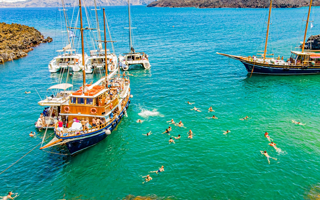 Guests swimming near boats in hot springs during Santorini volcanic cruise tour.