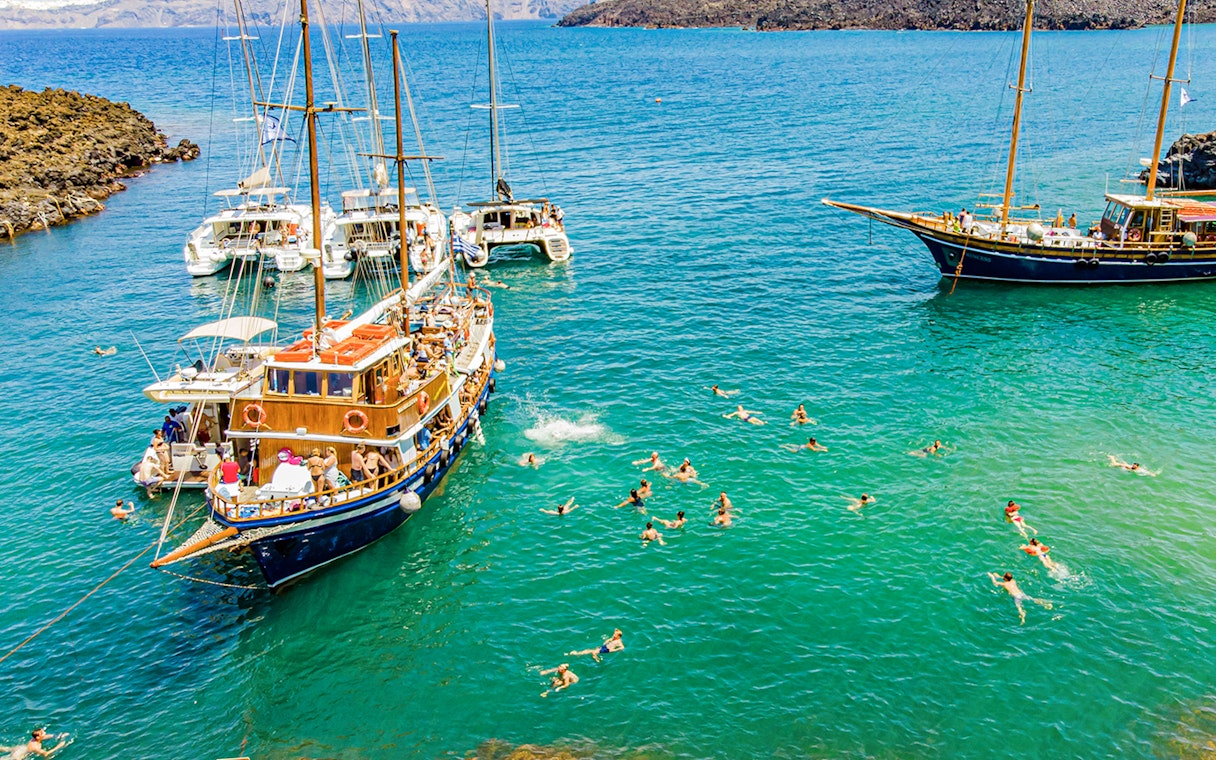 Guests swimming near boats in hot springs during Santorini volcanic cruise tour.