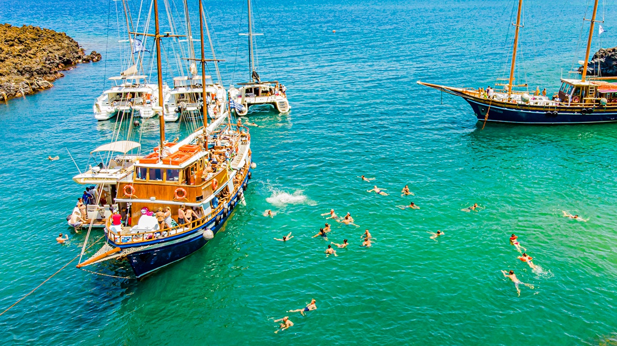 Guests swimming near boats in hot springs during Santorini volcanic cruise tour.