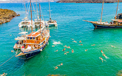 Guests swimming near boats in hot springs during Santorini volcanic cruise tour.
