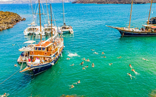 Guests swimming near boats in hot springs during Santorini volcanic cruise tour.