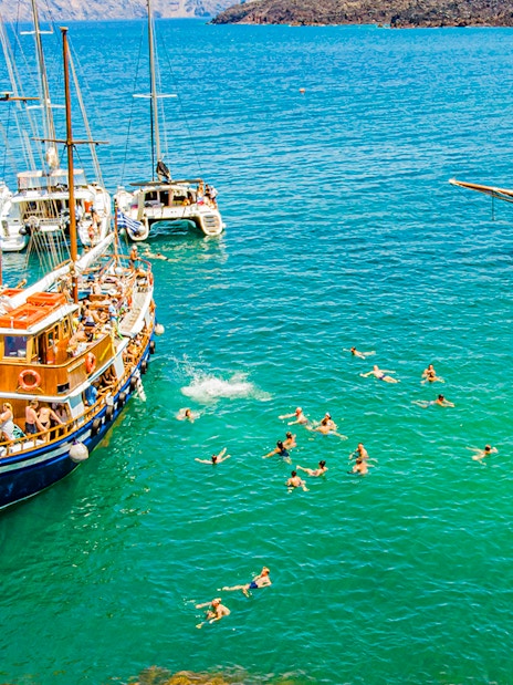 Guests swimming near boats in hot springs during Santorini volcanic cruise tour.
