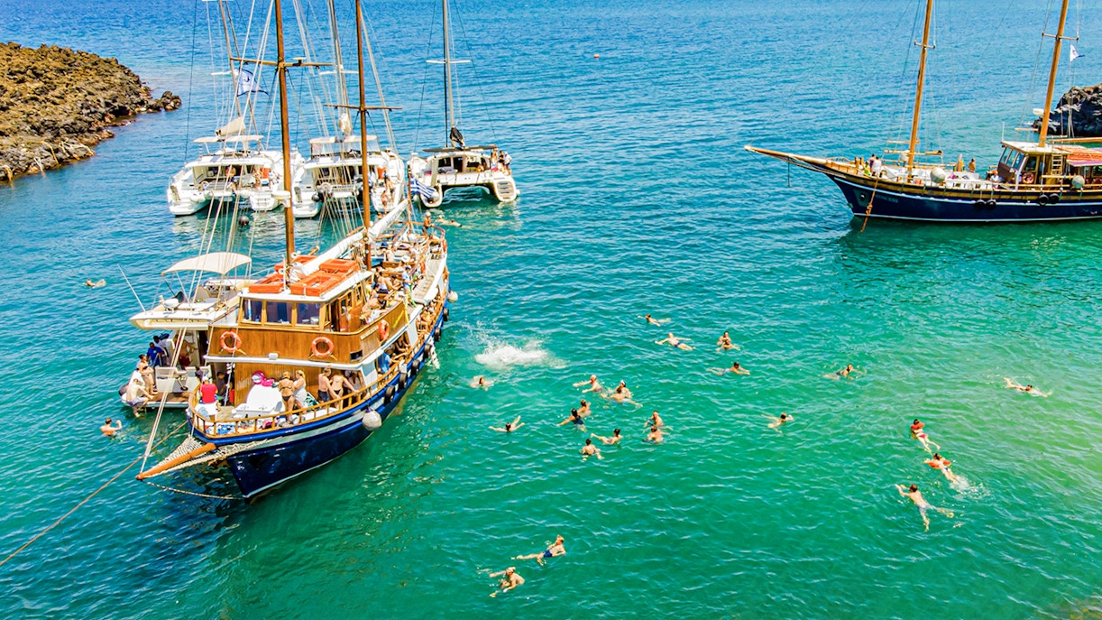 Guests swimming near boats in hot springs during Santorini volcanic cruise tour.