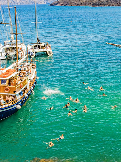 Guests swimming near boats in hot springs during Santorini volcanic cruise tour.