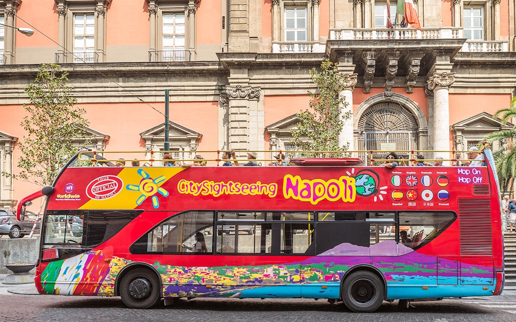 Open-top sightseeing bus in Naples in front of historic building.