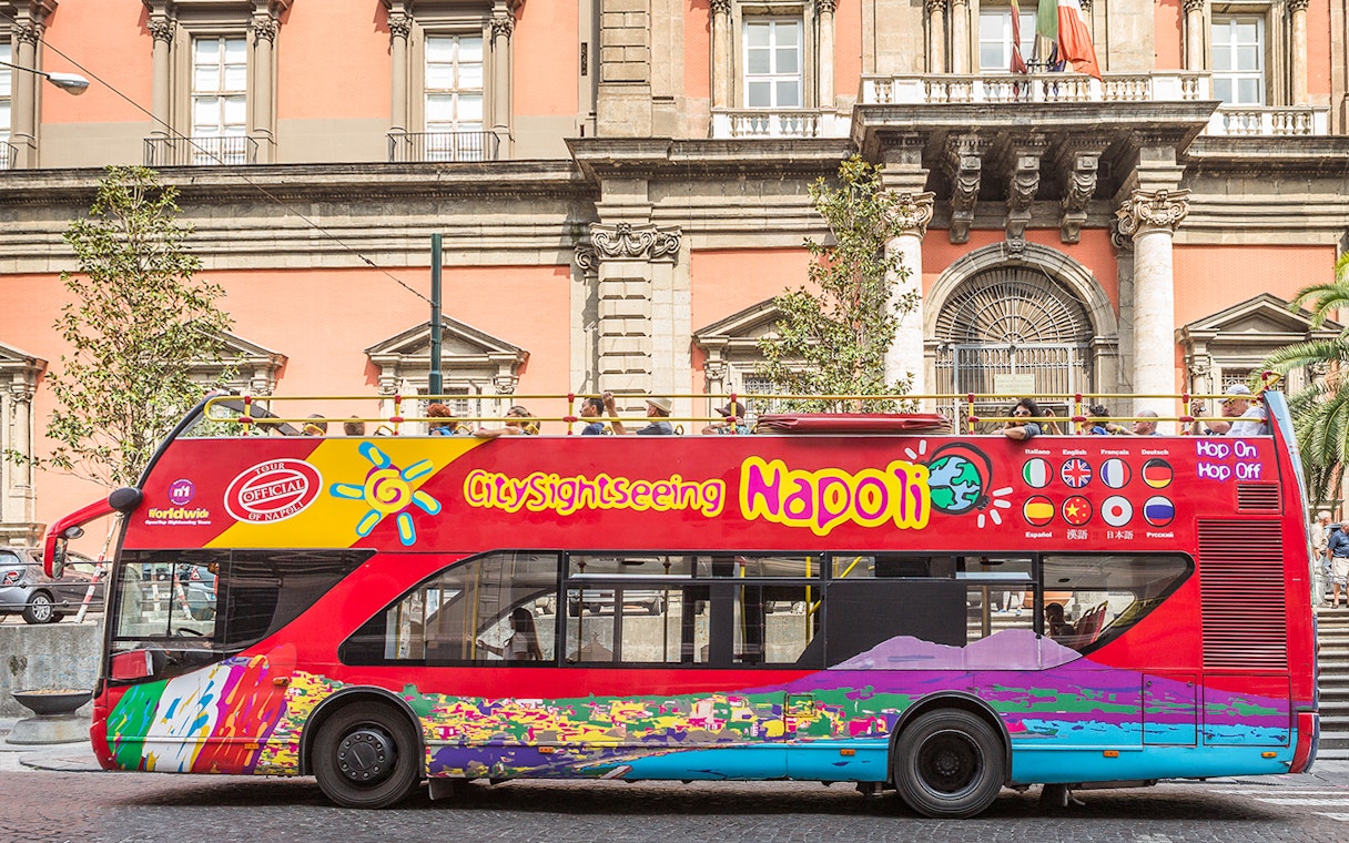 Open-top sightseeing bus in Naples in front of historic building.