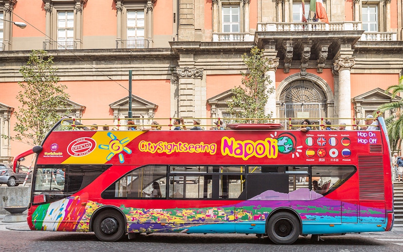 Open-top sightseeing bus in Naples in front of historic building.