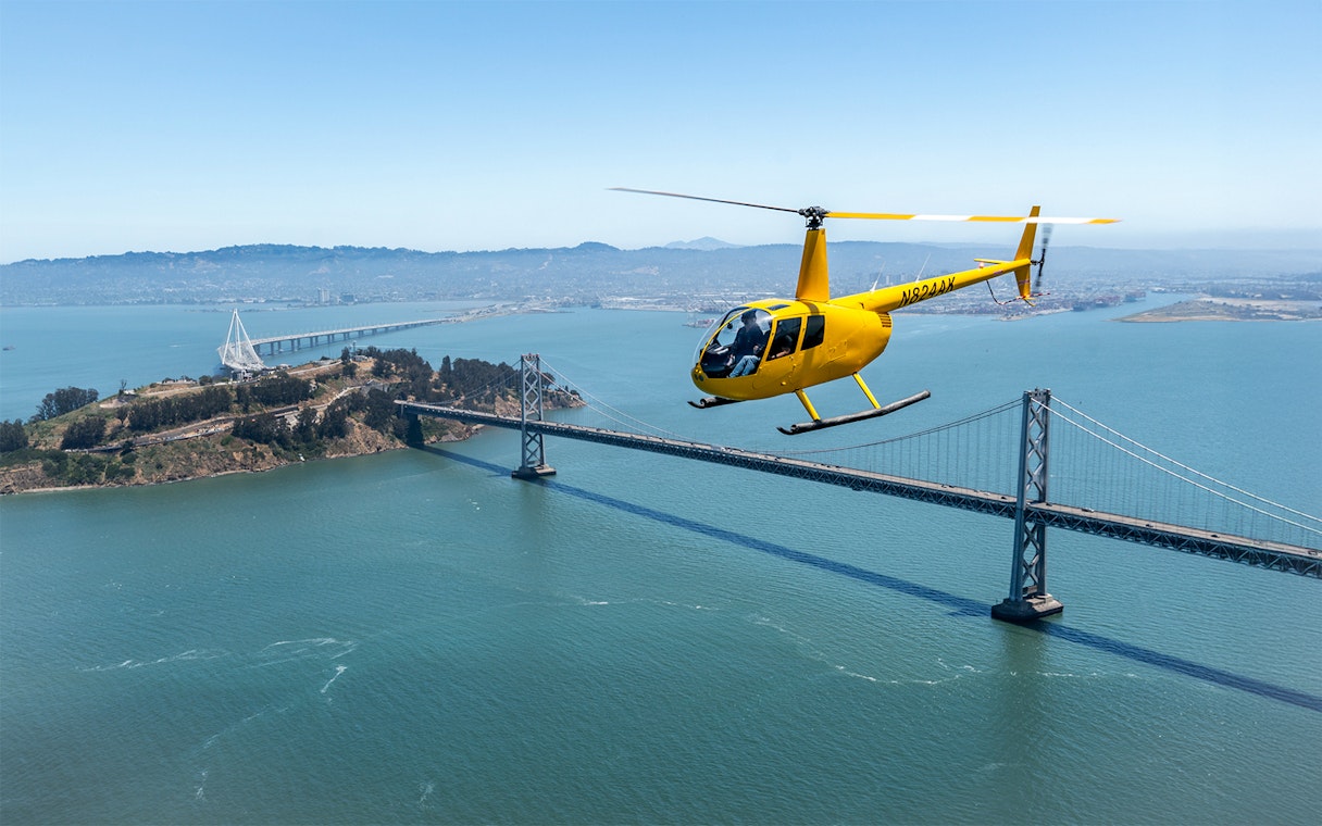 Yellow helicopter flying over Bay Bridge during Golden Gate Helicopter Tour.