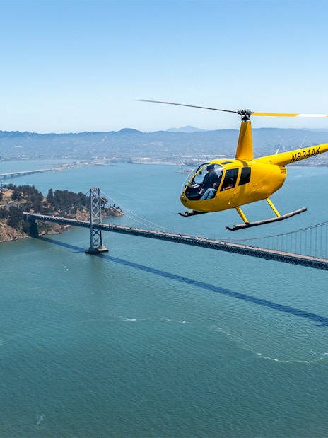 Yellow helicopter flying over Bay Bridge during Golden Gate Helicopter Tour.