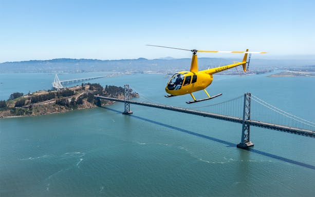 Yellow helicopter flying over Bay Bridge during Golden Gate Helicopter Tour.