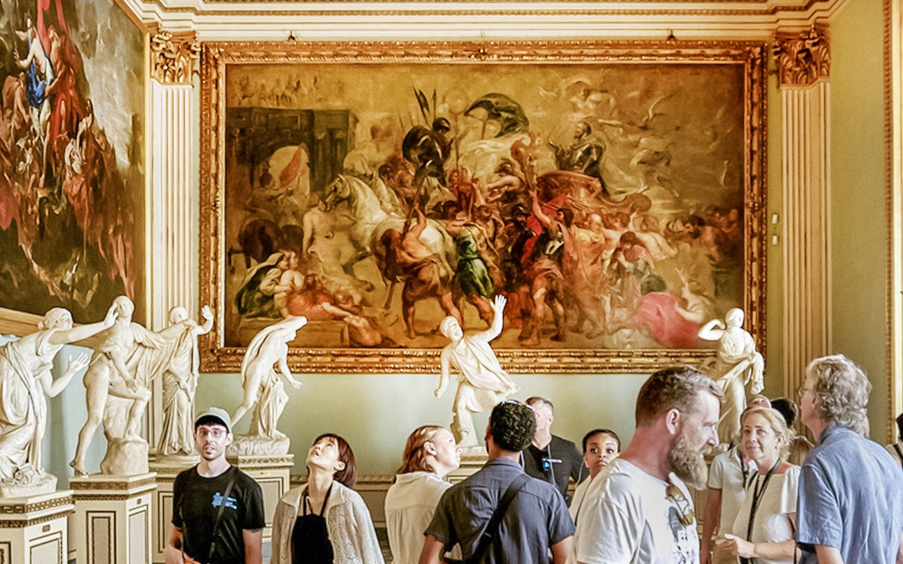 Visitors observing paintings and sculptures in the Rubens Niobe Room at Uffizi Gallery, Florence.