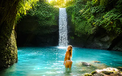 Person standing in turquoise pool beneath lush waterfall, Ubud, Bali.