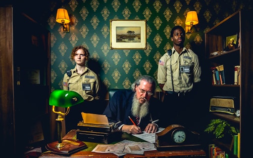 Prison-themed bar scene with guards and a man writing at a desk, Alcotraz experience.