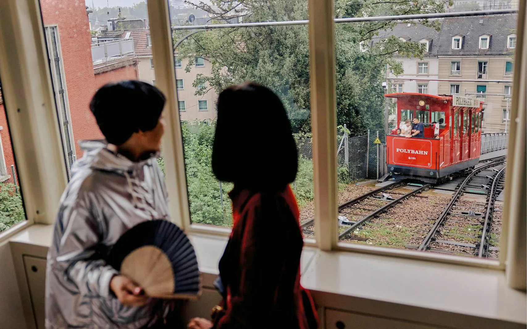 Red Polybahn funicular tram in Zurich viewed from inside a building, with two people looking out.