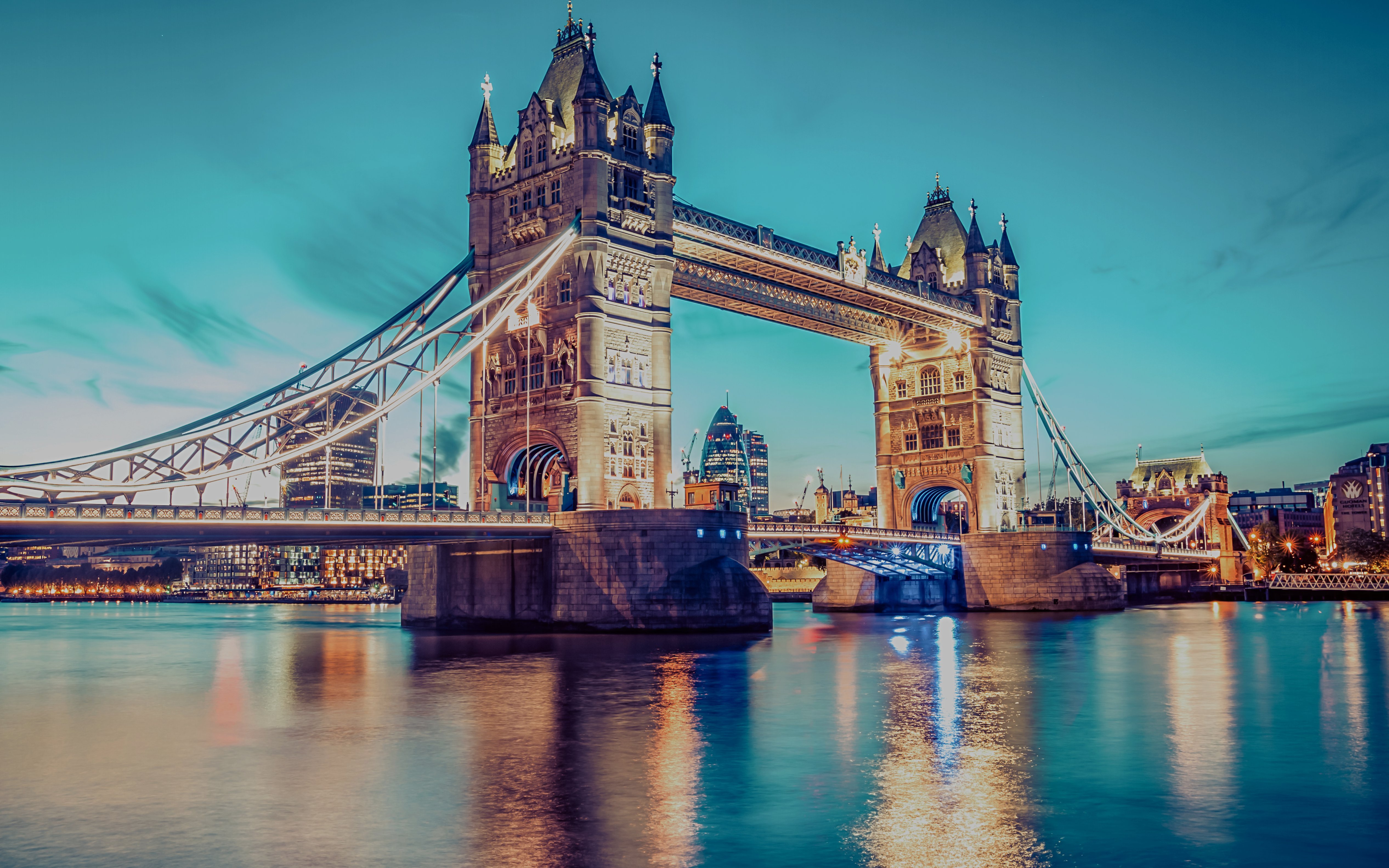 Tower Bridge in London illuminated at dusk, reflecting on the River Thames.