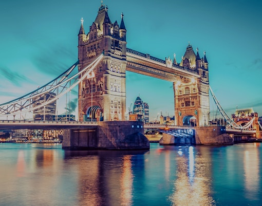 Tower Bridge in London illuminated at dusk, reflecting on the River Thames.