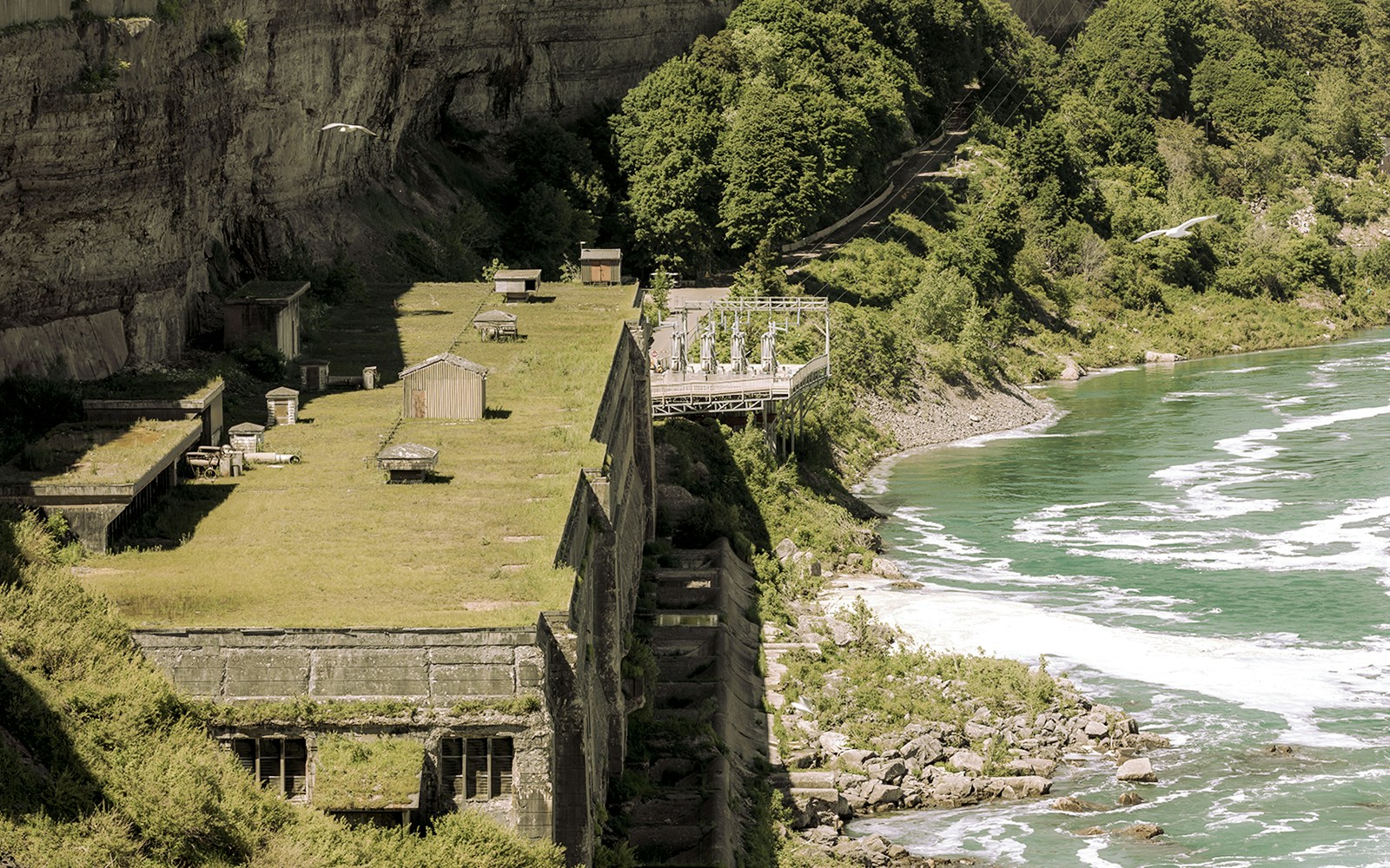 Old abandoned hydroelectric generating plant by a river with lush greenery.