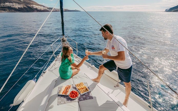 Tourists enjoying drinks on a private sailboat with snacks, ocean view, Tenerife coast.