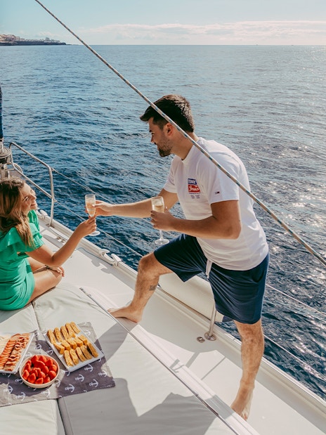 Tourists enjoying drinks on a private sailboat with snacks, ocean view, Tenerife coast.