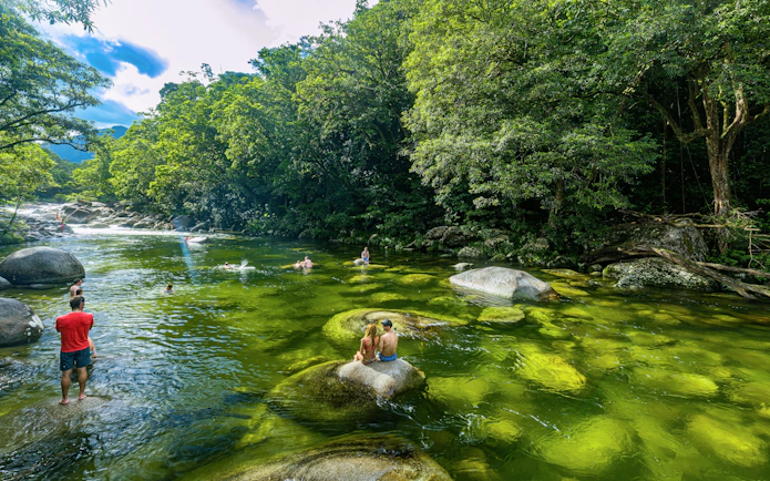 Visitors swimming in Mossman Gorge River, surrounded by lush rainforest in Daintree National Park, Queensland.