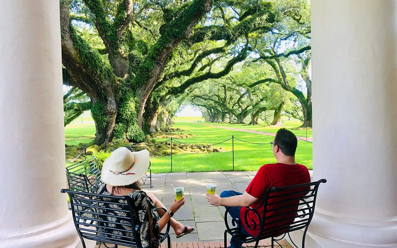 Visitors relaxing on a porch overlooking oak trees at Oak Alley Plantation, New Orleans.
