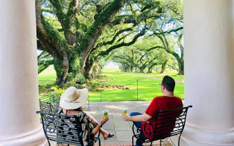 Visitors relaxing on a porch overlooking oak trees at Oak Alley Plantation, New Orleans.