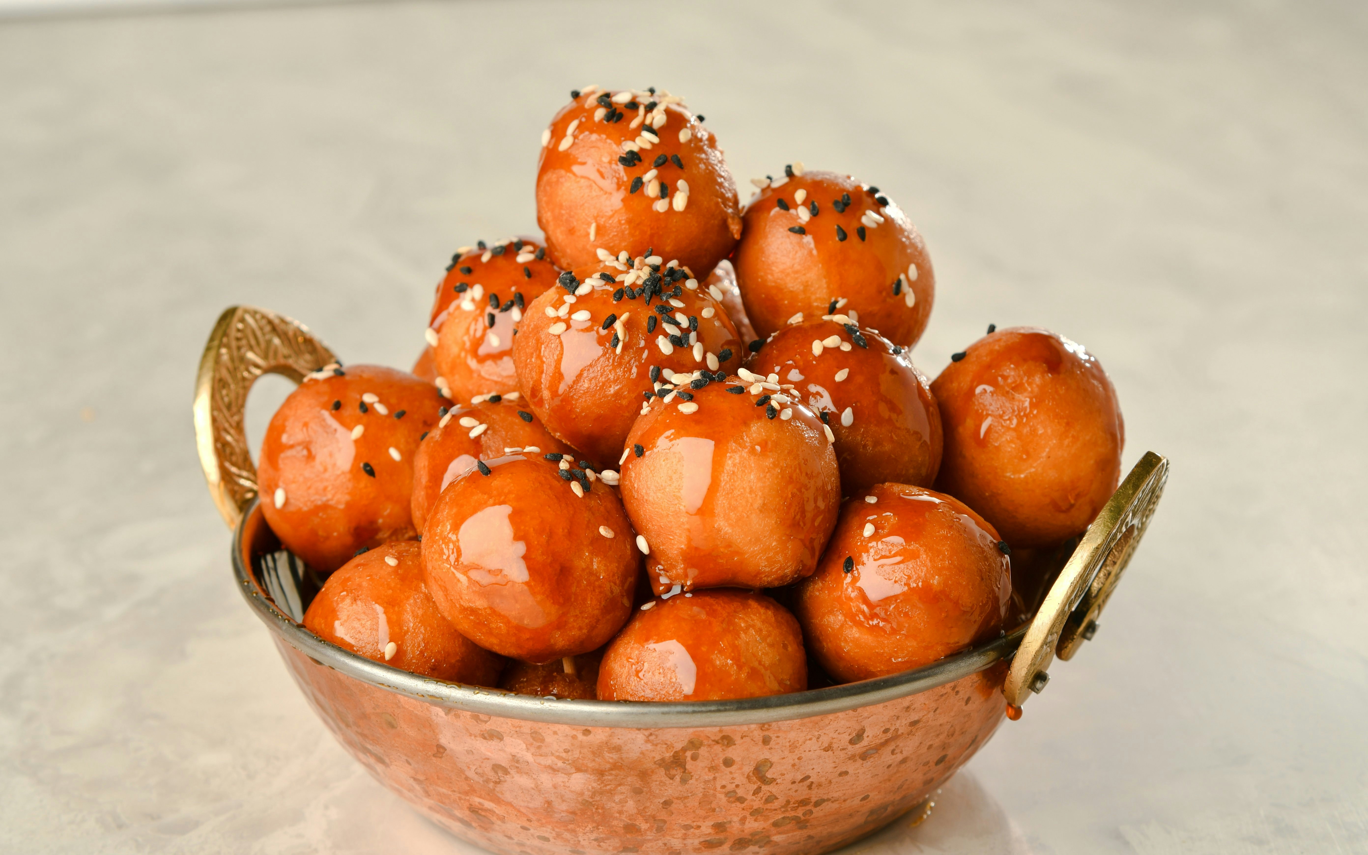 Luqaimat topped with sesame seeds and drizzled with date syrup in a decorative bowl.