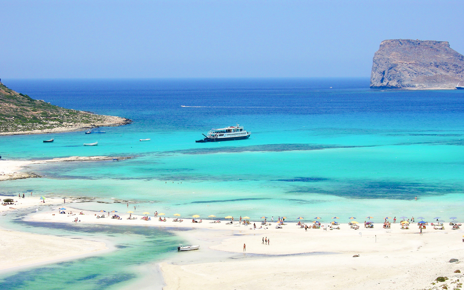 Cruise ship near Balos Island with beachgoers on sandy shore.